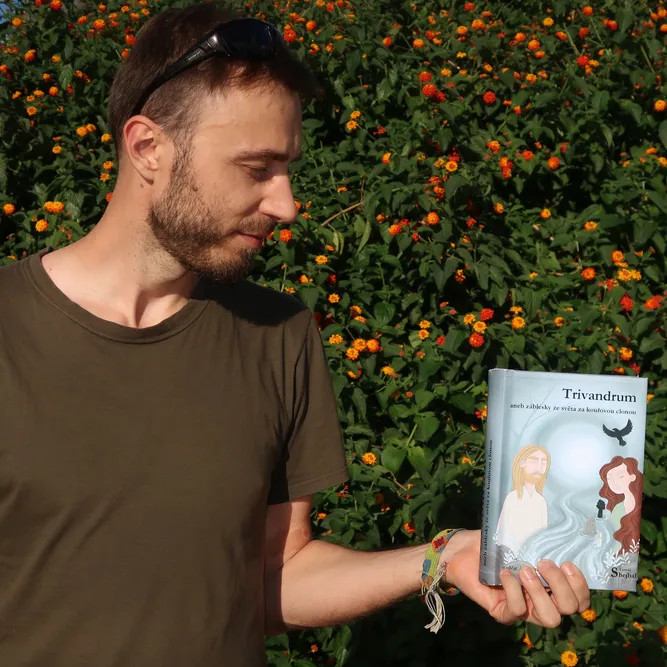 Autor románu Trivandrum kouká na knihu, na pozadí keř s oranžovými květy